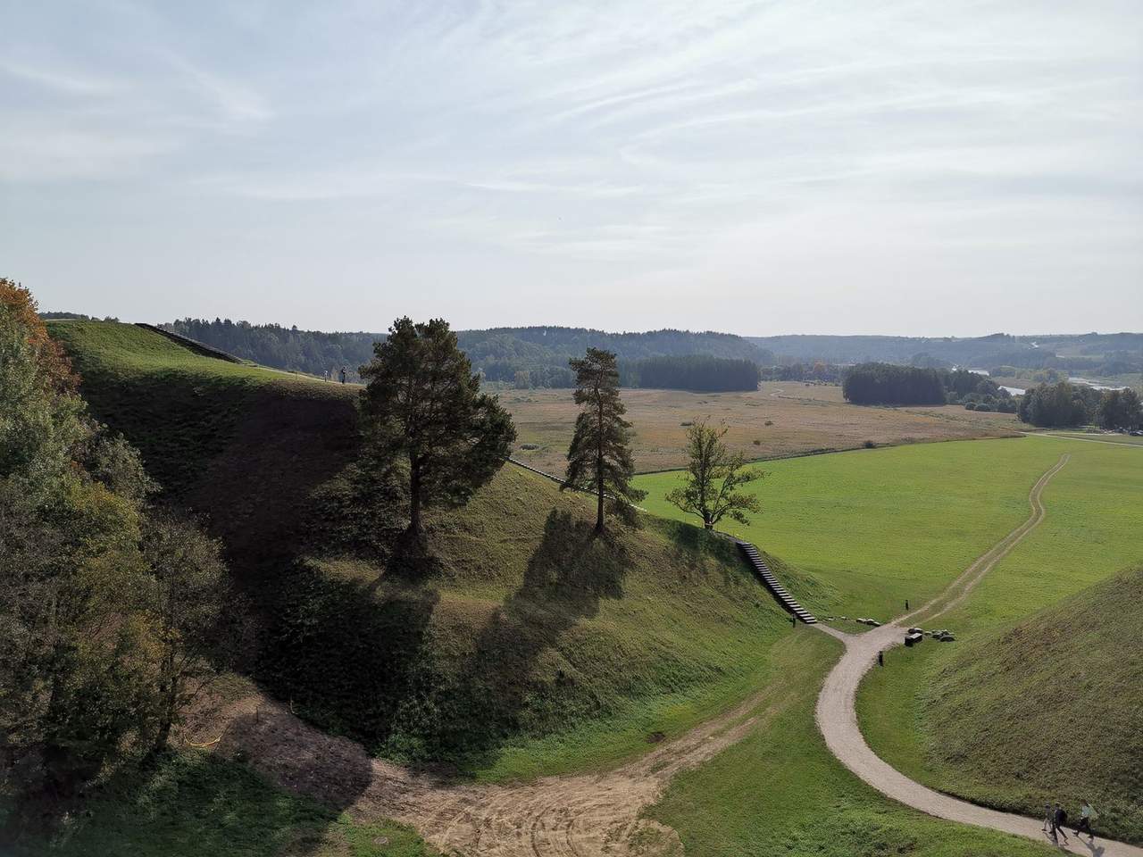Žoliniai Kernavės piliakalniai su laiptais ir plati Neries slėnio panorama po šviesiu dangumi